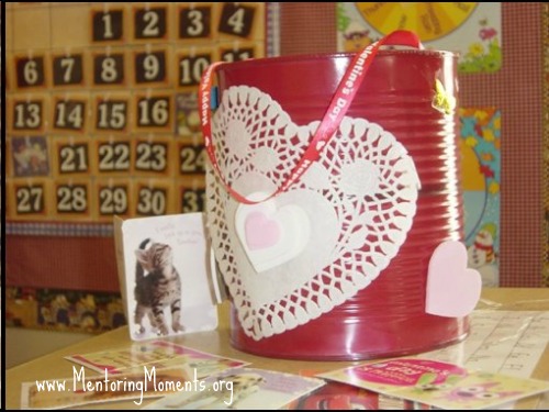 Coffee can painted red with white heart shaped doily adhered to front. Ribbon glued to inside of can to make a handle.