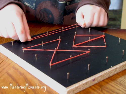 View of a child's hands placing rubber bands in geometric shapes on a geoboard.