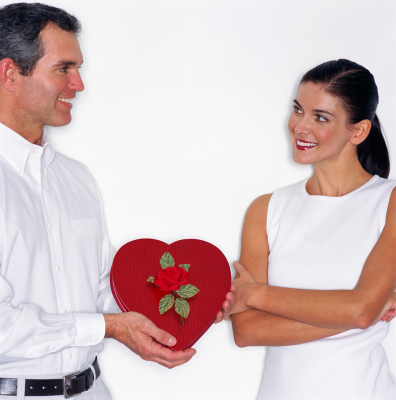 Husband presenting red heart shaped box of Valentine Day's chocolates to wife