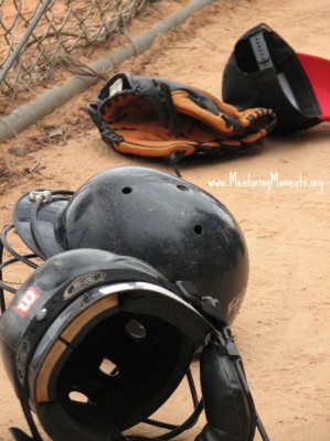 Baseball hat, batting helmets, and mitt laying beside fence. www.MentoringMoments.org