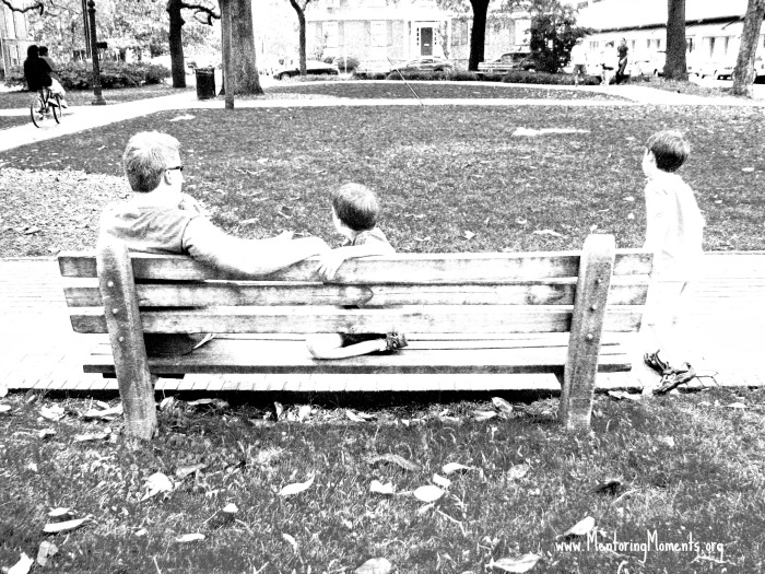 Father and sons sitting on a park bench.